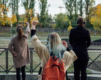 Menschen mit Kopfhörern stehen vor einem Geländer im Park und recken die Faust.