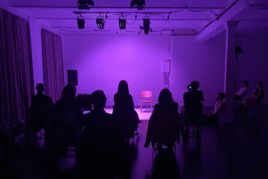 TATWERK Aufnahme einer in Violett beleuchteten Bühne. Die Bühne, die hinter dem Publikum zu sehen ist, ist leer.