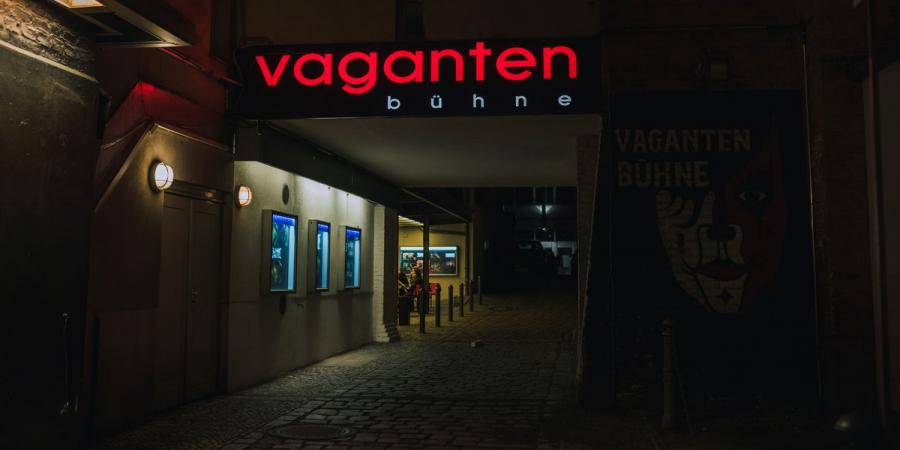 Auf dem Foto ist der Zugang zur Vaganten Bühne bei Nacht zu sehen. Über dem Durchgang des Hinterhofs leuchtet der Vaganten-Schriftzug in roten Buchstaben.